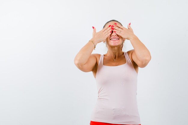 Junge Frau im Unterhemd, das Augen mit Händen schließt und niedlich, Vorderansicht schaut.