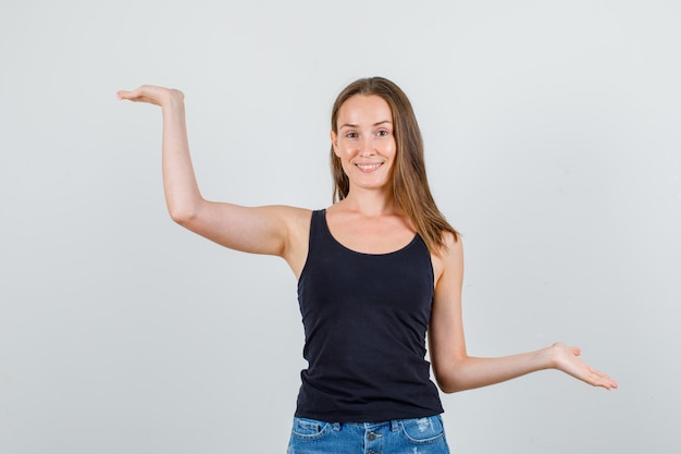 Junge Frau im Unterhemd, Shorts, die Handflächen offen halten und fröhlich aussehen