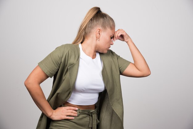 Junge Frau im weißen Hemd, das sich an grauer Wand schmerzt.