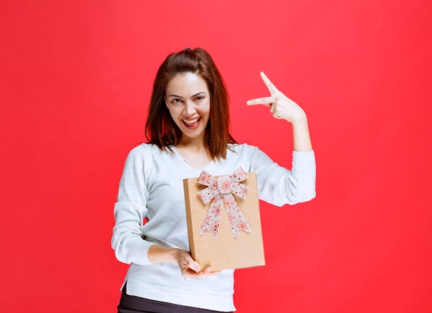 Junge Frau im weißen Hemd, die eine Geschenkbox aus Karton hält und ein positives Handzeichen zeigt