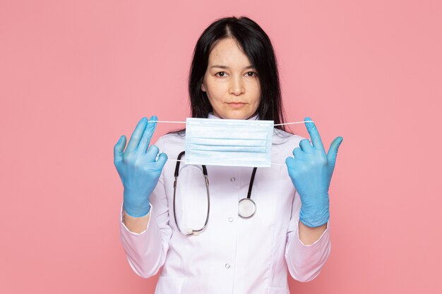 junge Frau im weißen medizinischen Anzug blaue Handschuhe mit Stethoskop auf rosa