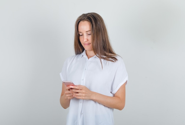Junge Frau im weißen T-Shirt, das Smartphone verwendet und beschäftigt schaut