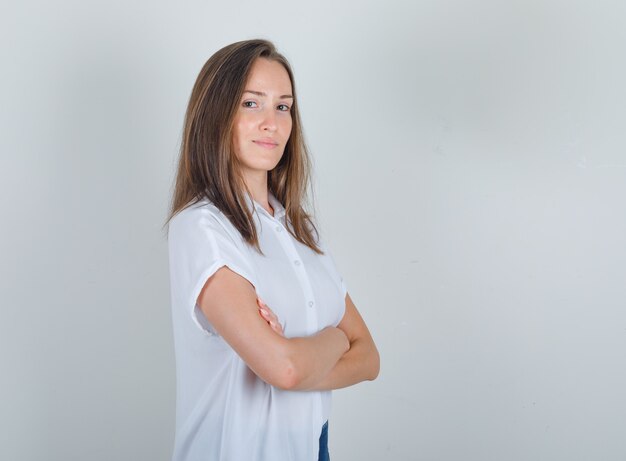 Junge Frau im weißen T-Shirt, Jeans, die mit verschränkten Armen stehen und fröhlich schauen.