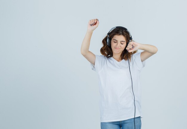 Junge Frau im weißen T-Shirt, Jeans, die Musik mit Kopfhörern genießen und munter, Vorderansicht schauen.