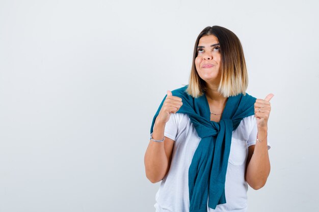 Junge Frau im weißen T-Shirt zeigt Daumen hoch und sieht attraktiv aus, Vorderansicht.