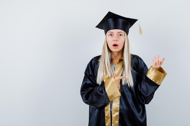 Junge Frau in Absolventenuniform, die zur Seite zeigt und überrascht aussieht