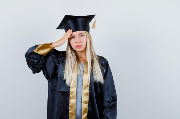 Junge Frau in Absolventenuniform mit starken Kopfschmerzen und unwohlem Aussehen,