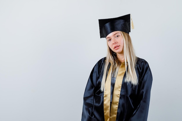 Junge Frau in Absolventenuniform posiert, während sie in die Kamera schaut und vernünftig aussieht