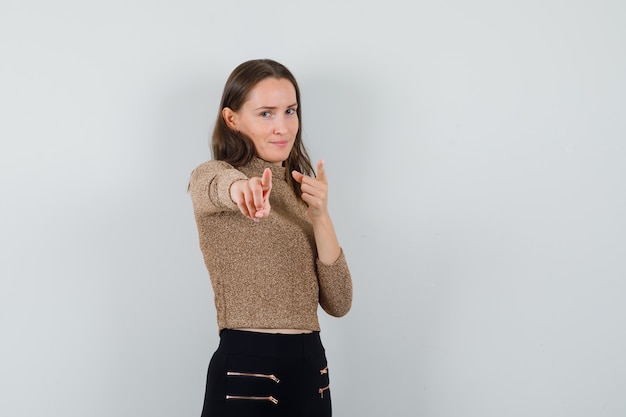 Junge Frau in Bluse, Rock zeigt auf Kamera und schaut selbstbewusst, Vorderansicht. Platz für Text