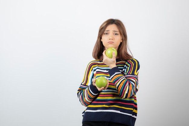 Junge Frau in der Freizeitkleidung, die mit grünen Äpfeln auf weißem Hintergrund steht.