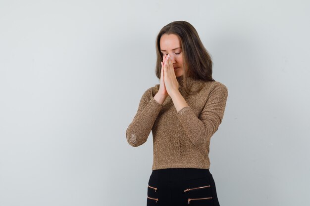 Junge Frau in der goldenen Bluse betend und hoffnungsvoll schauend, Vorderansicht.