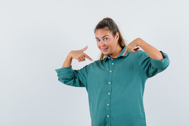 Junge Frau in der grünen Bluse, die auf sich selbst zeigt und glücklich schaut