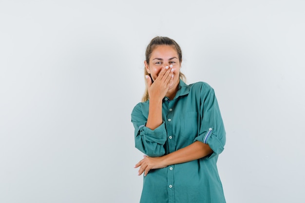 Junge Frau in der grünen Bluse, die Mund mit Hand bedeckt, während lachend und niedlich aussehend