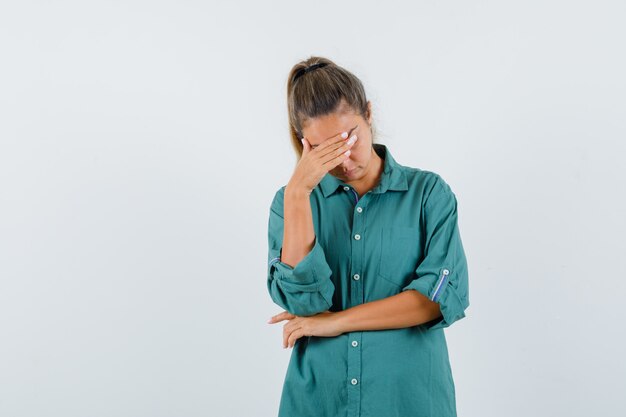 Junge Frau in der grünen Bluse, die Stirn mit Hand bedeckt und ernst schaut