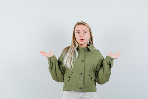 Junge Frau in der grünen Jacke, Jeans, die hilflose Geste zeigen, Vorderansicht.