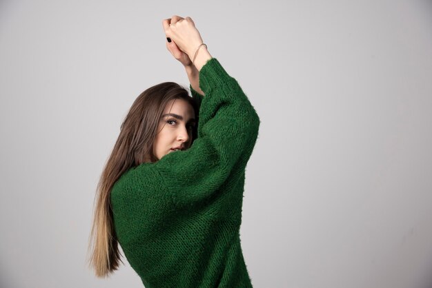 Junge Frau in der grünen Strickjacke, die auf Grau aufwirft.