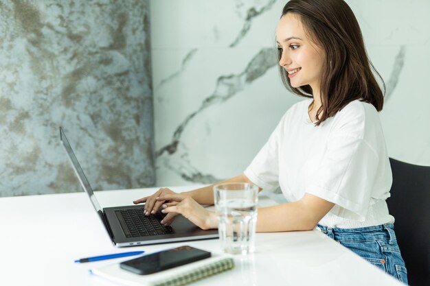 Junge Frau in der Küche Beeren essend und Laptop verwendend. Glückliche Frau, die Laptop beim Stehen in der Küche morgens betrachtet.