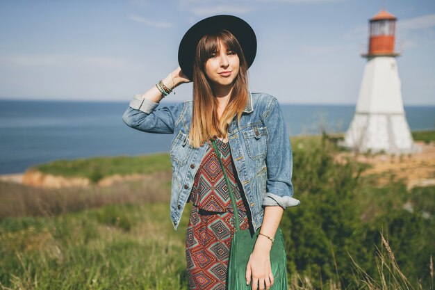 Junge Frau in der Natur, Leuchtturm, böhmisches Outfit, Jeansjacke, schwarzer Hut, lächelnd, glücklich, Sommer, stilvolle Accessoires