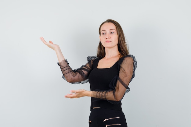 Junge Frau in der schwarzen Bluse, die ihre Hände mit offenen Handflächen beiseite hebt und konzentriert schaut