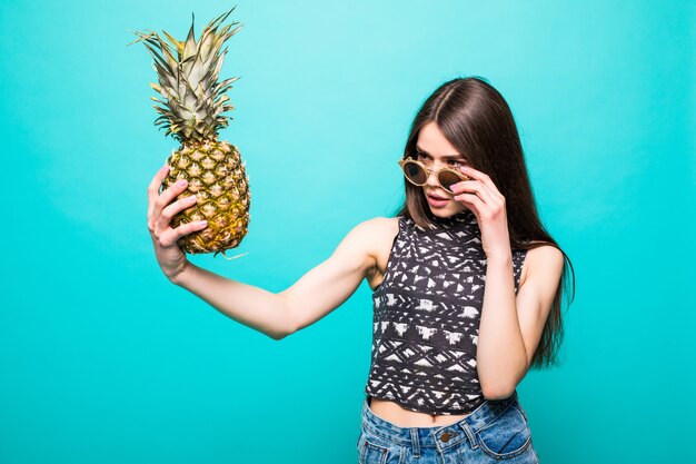 Junge Frau in der Sonnenbrillen-Freizeitkleidung mit Ananas in den Händen lokalisiert