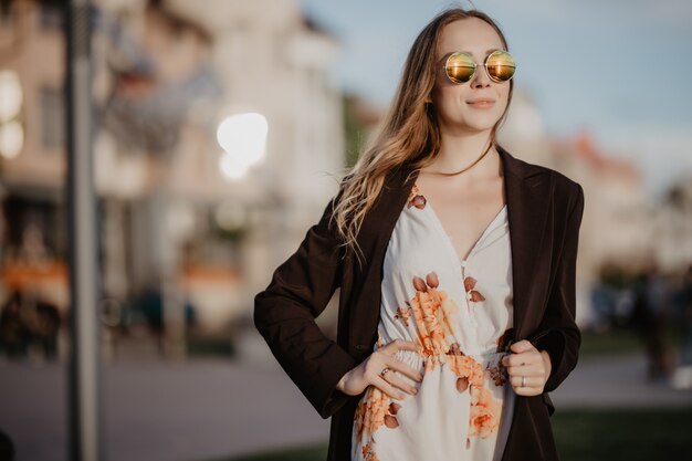 Junge Frau in der trendigen Sonnenbrille und im weißen Poloshirt an einem Frühlingstag bei Sonnenuntergang