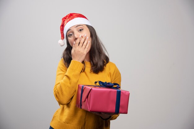 Junge Frau in der Weihnachtsmütze, die eine Geschenkbox hält.