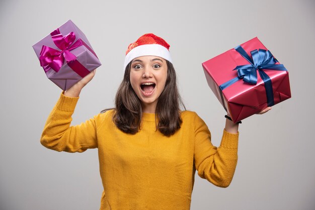 Junge Frau in der Weihnachtsmütze, die Geschenkboxen hält und sich glücklich fühlt.