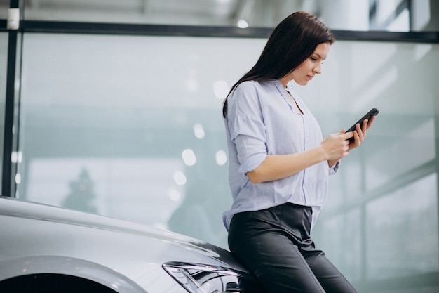 Junge Frau in einem Autoshowraum unter Verwendung des Telefons