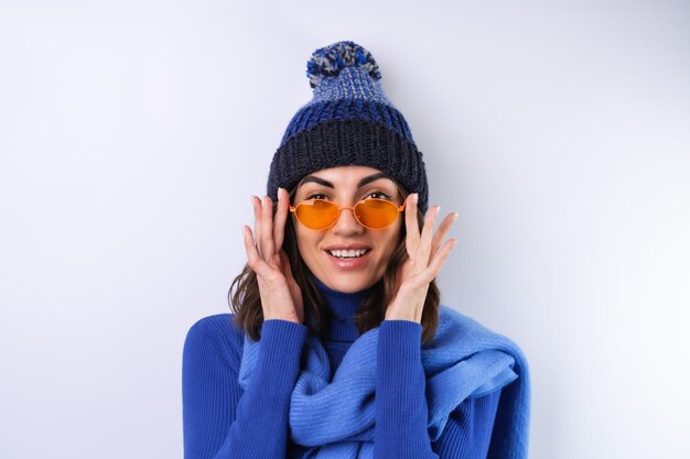 Junge Frau in einem blauen Golfrollkragenhut und in einer Schalsonnenbrille auf einem weißen Hintergrund fröhlich in einer guten Laune