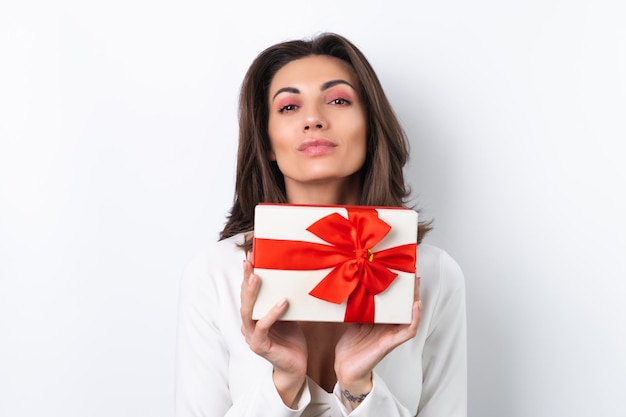 Junge Frau in einem Cocktailkleid Goldkette leuchtend frühlingsrosa Make-up auf weißem Hintergrund Hält eine Geschenkbox für den 8. März und lächelt fröhlich