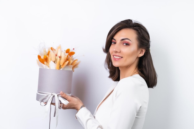 Junge Frau in einem Cocktailkleid Goldkette leuchtend frühlingsrosa Make-up auf weißem Hintergrund Hält einen Strauß orangefarbener Trockenblumen als Geschenk für den 8. März