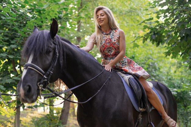 Junge Frau in einem hellen bunten Kleid, das ein schwarzes Pferd reitet