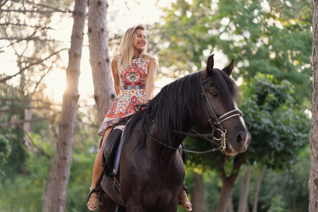 Junge Frau in einem hellen bunten Kleid, das ein schwarzes Pferd reitet