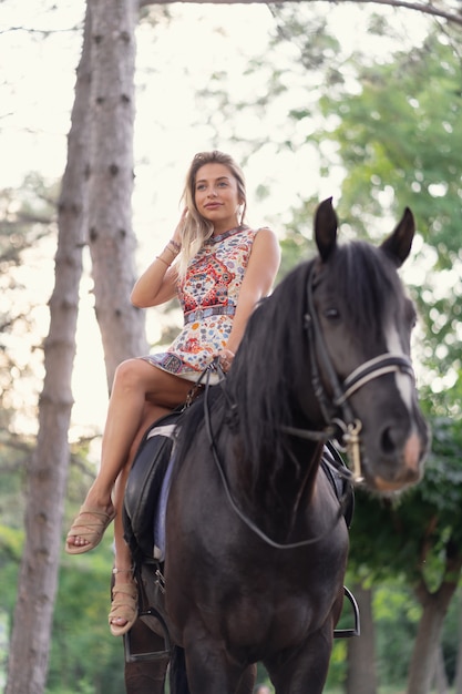 Kostenloses Foto junge frau in einem hellen bunten kleid, das ein schwarzes pferd reitet