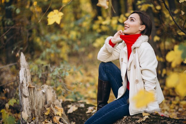 Junge Frau in einem Herbstpark, der auf einem Klotz sitzt