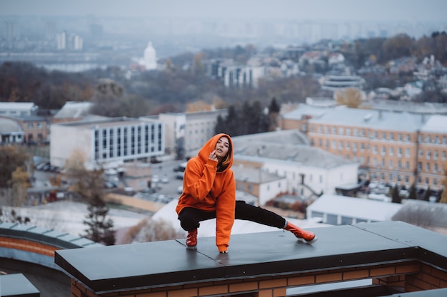 Junge Frau in einem orange Sweatshirt wirft auf dem Dach eines Gebäudes in der Innenstadt auf