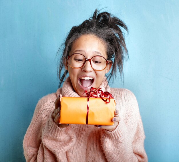 Junge Frau in einem rosa Pullover, der Glück ausdrückt, während sie eine Geschenkbox hält