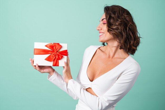 Junge Frau in einem weißen Abendkleid auf hellgrün mit leuchtend rosa Make-up, die eine Geschenkbox hält