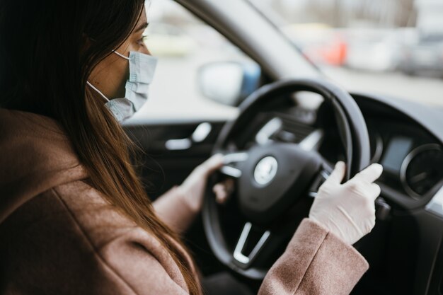 Junge Frau in einer Maske und Handschuhen, die ein Auto fahren.
