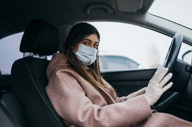 Junge Frau in einer Maske und Handschuhen, die ein Auto fahren.