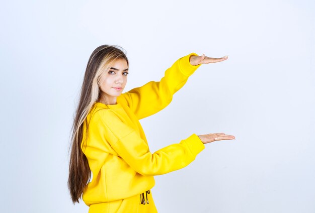 Junge Frau in gelber Jogginghose und Hoodie, die auf weißer Wand steht