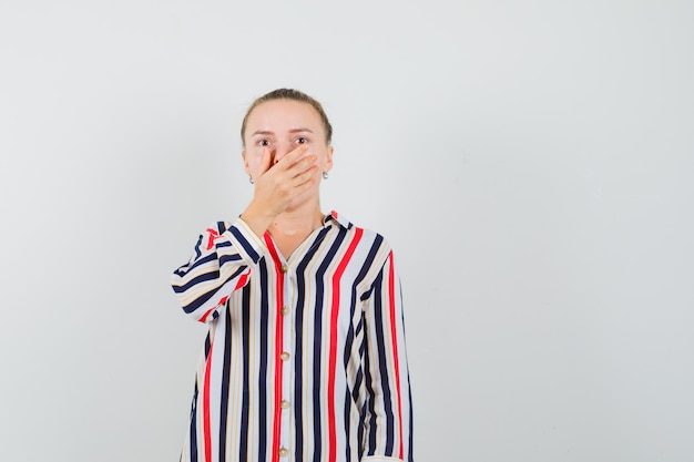 Junge Frau in gestreifter Bluse, die ihren Mund mit beiden Händen bedeckt und überrascht aussieht