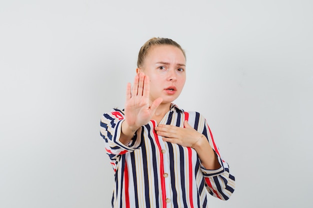 Kostenloses Foto junge frau in gestreifter bluse, die stoppgeste zeigt und erschrocken aussieht