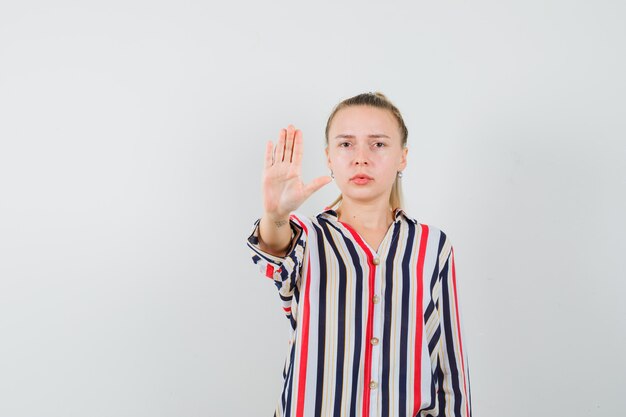 Junge Frau in gestreifter Bluse, die Stoppgeste zeigt und wütend aussieht