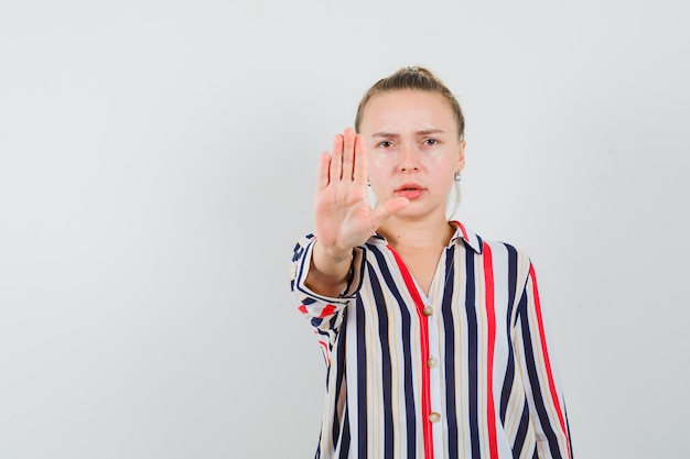 Junge Frau in gestreifter Bluse, die Stoppschild zeigt und wütend schaut