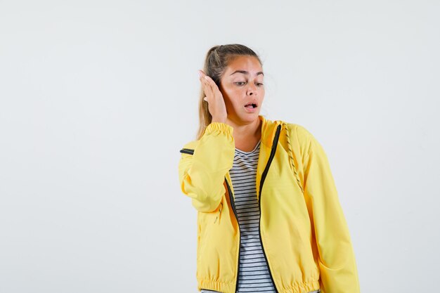 Junge Frau in Jacke, T-Shirt, das Hand am Ohr hält und schön schaut, Vorderansicht.