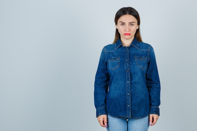 Junge Frau in Jeanshemd und Jeans, die vorne schauen und beleidigt schauen