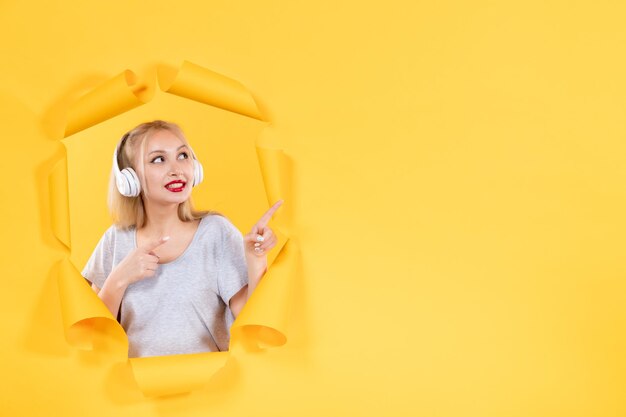 Junge Frau in Kopfhörern auf dem zerrissenen gelben Papierhintergrundaudio-Ultraschallmusikton