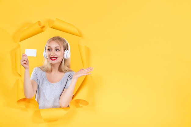 Junge Frau in Kopfhörern mit Kreditkarte auf gelbem Hintergrund Ultraschall-Audiomusik