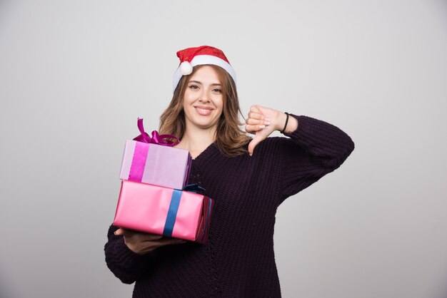 Junge Frau in Nikolausmütze mit Geschenkboxen, die einen Daumen nach unten zeigen.